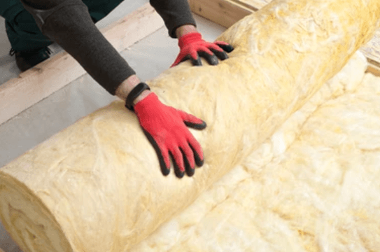An imagine of a working man in a blue jumpsuit rolling out loft insulation in a retrofitted home