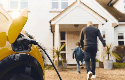 An electrical vehicle charger plugged into a family home as a family walk into their retrofitted home